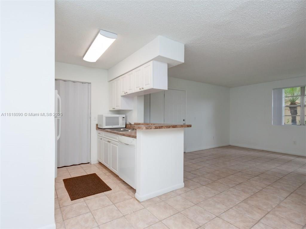A kitchen with white cabinets and a breakfast bar opens into a tiled living area — 1235 SW 46th Ave # 707, Pompano Beach FL 33069, POMPANO BEACH, FL