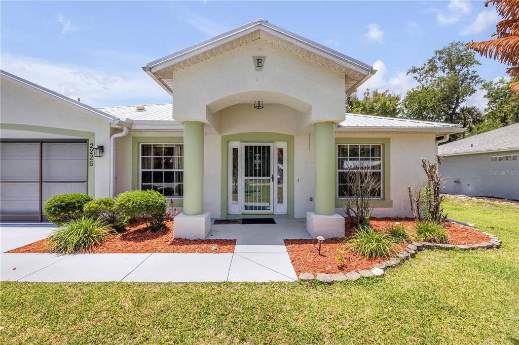 A single-story house features a covered entryway with two columns and a metal roof — 2226 JUNIPER DRIVE, EDGEWATER, FL