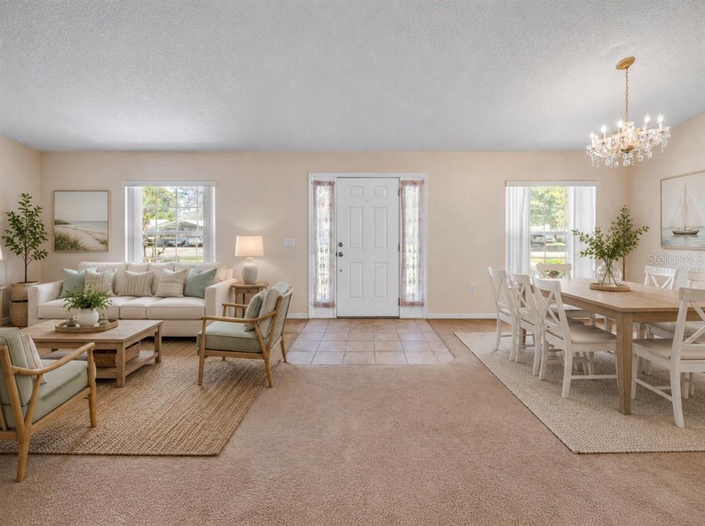 A living and dining room with beige carpet, a white front door, and a chandelier — 2226 JUNIPER DRIVE, EDGEWATER, FL