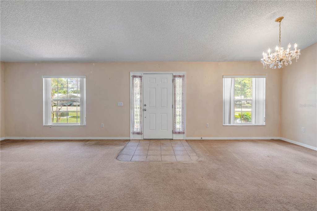 A living room with beige carpet, a tiled entryway, two windows, and a crystal chandelier — 2226 JUNIPER DRIVE, EDGEWATER, FL