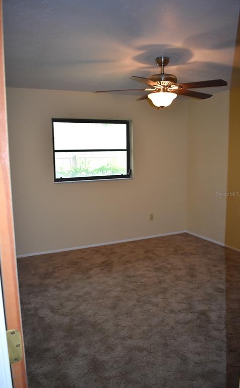 A bedroom with beige walls, brown carpet, a ceiling fan, and a single window — 147 HOURGLASS DRIVE, VENICE, FL