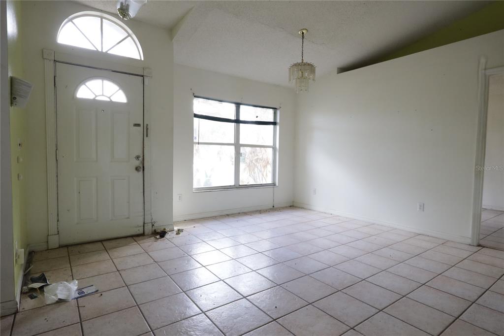 An empty room with white walls, tile flooring, a front door, and a chandelier — 11346 CYPRESS LEAF DR. DRIVE, ORLANDO, FL