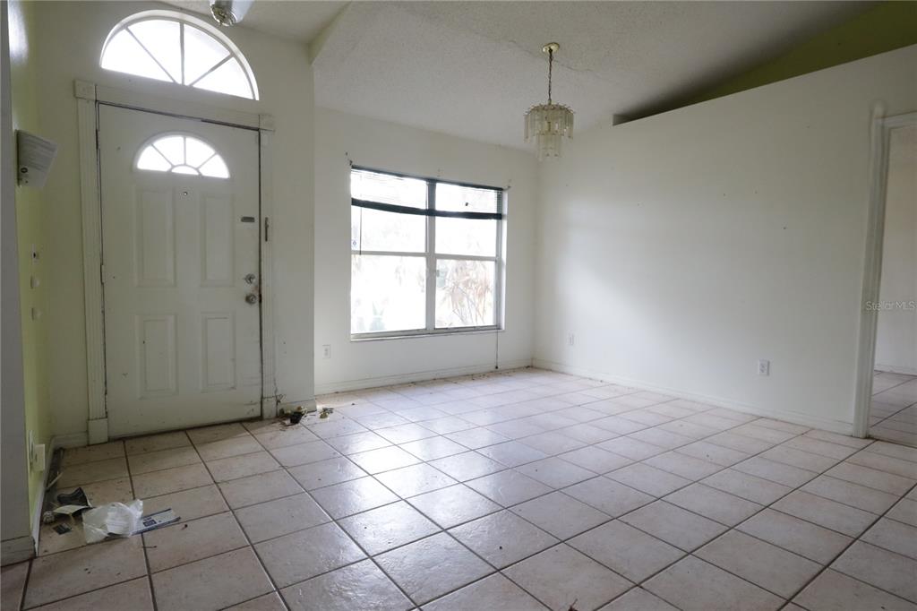 An empty room features white walls, tile flooring, a front door, and a hanging chandelier — 11346 CYPRESS LEAF DR. DRIVE, ORLANDO, FL