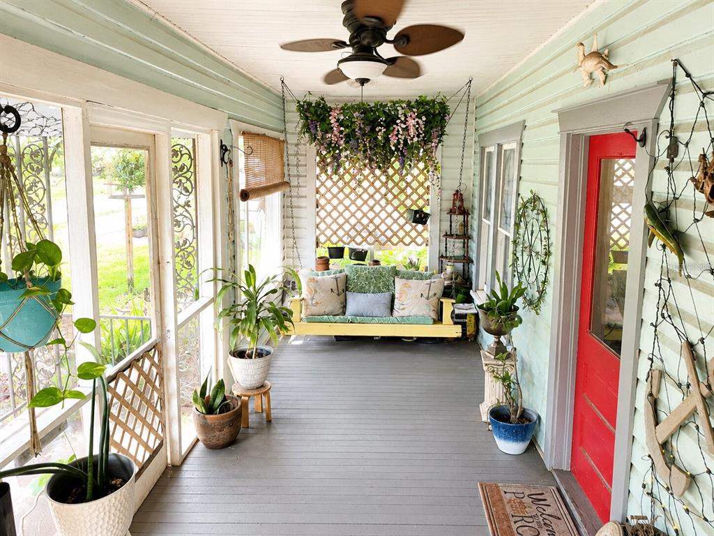 A covered porch features a hanging swing, potted plants, a ceiling fan, and a red door — 129 S MILLS AVENUE, ARCADIA, FL