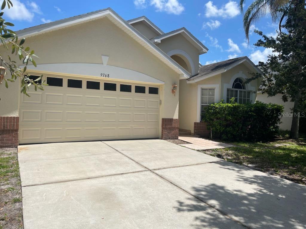 A beige single-story house features a two-car garage, brick accents, and a concrete driveway — 9768 DORIATH CIRCLE, ORLANDO, FL