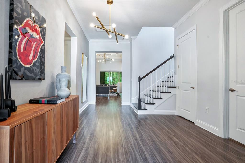 A modern entryway features wood-look flooring, a wooden console table, a staircase, and a chandelier — 10654 ROYAL CYPRESS WAY, ORLANDO, FL