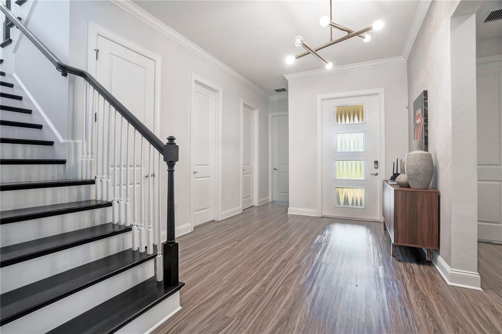 A bright entryway features wood-look flooring, a staircase with dark treads, and a modern chandelier — 10654 ROYAL CYPRESS WAY, ORLANDO, FL
