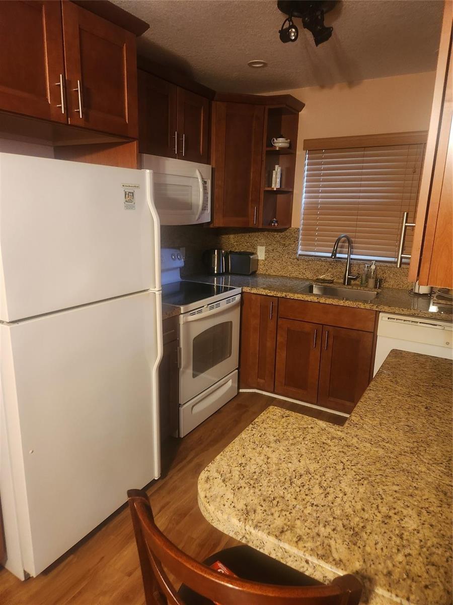 A kitchen features wood cabinets, granite countertops, white appliances, and a stainless steel sink — 237 Farnham J # 237, Deerfield Beach FL 33442, DEERFIELD BEACH, FL