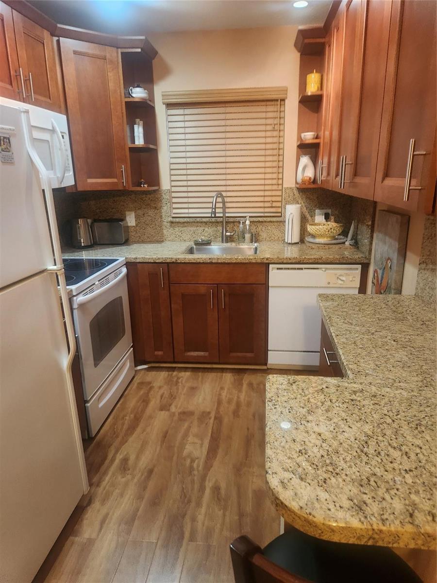 A kitchen features wood cabinets, granite countertops, stainless steel appliances, and wood-look flooring — 237 Farnham J # 237, Deerfield Beach FL 33442, DEERFIELD BEACH, FL