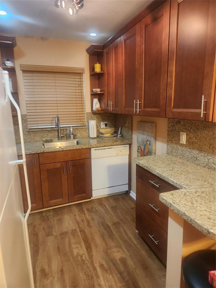 A kitchen features wood cabinets, granite countertops, a white dishwasher, and wood-look flooring — 237 Farnham J # 237, Deerfield Beach FL 33442, DEERFIELD BEACH, FL