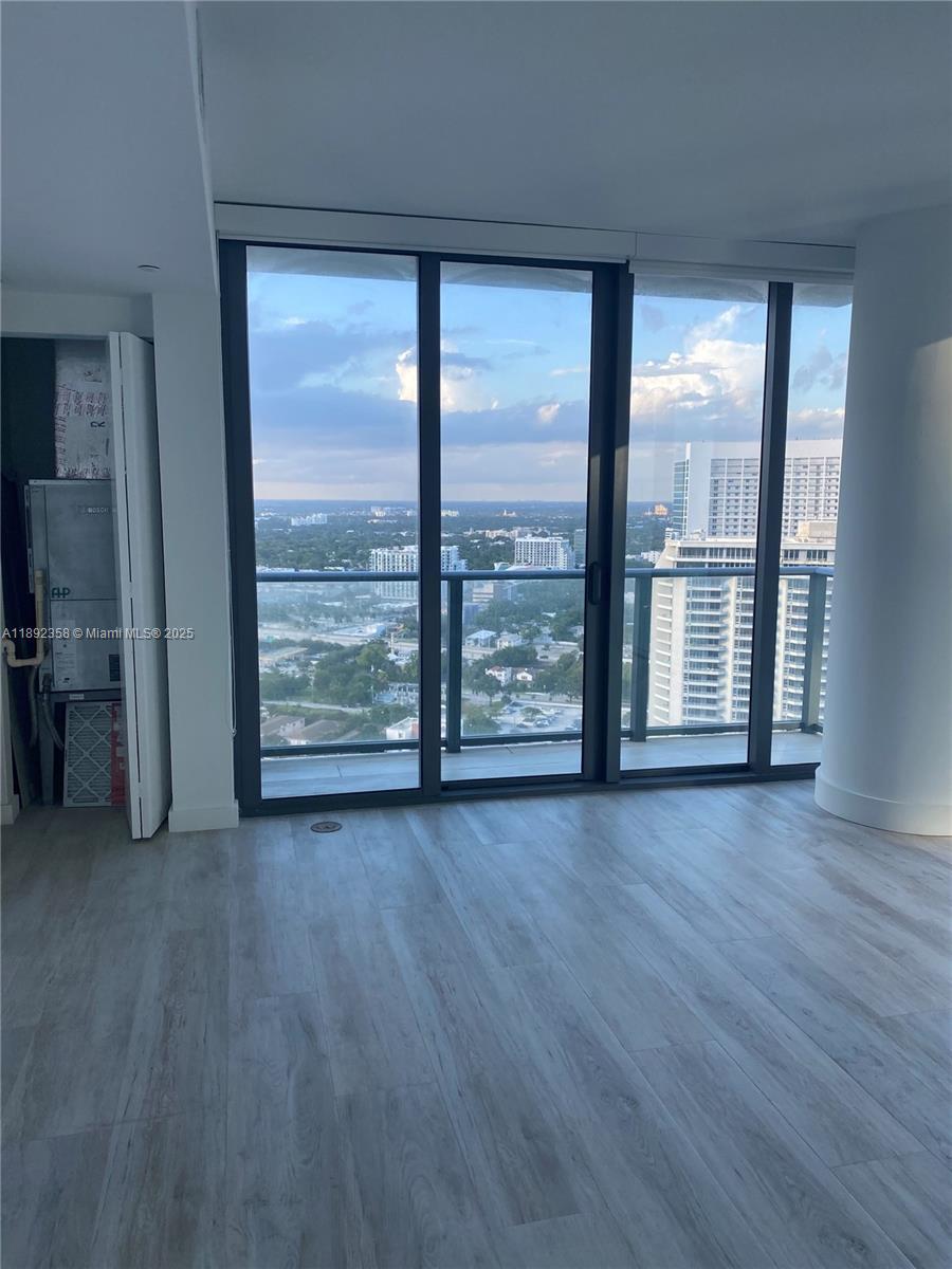 A room with light wood-look flooring features floor-to-ceiling windows overlooking a city skyline — 650 NE 32nd St # 3108, Miami FL 33137, MIAMI, FL