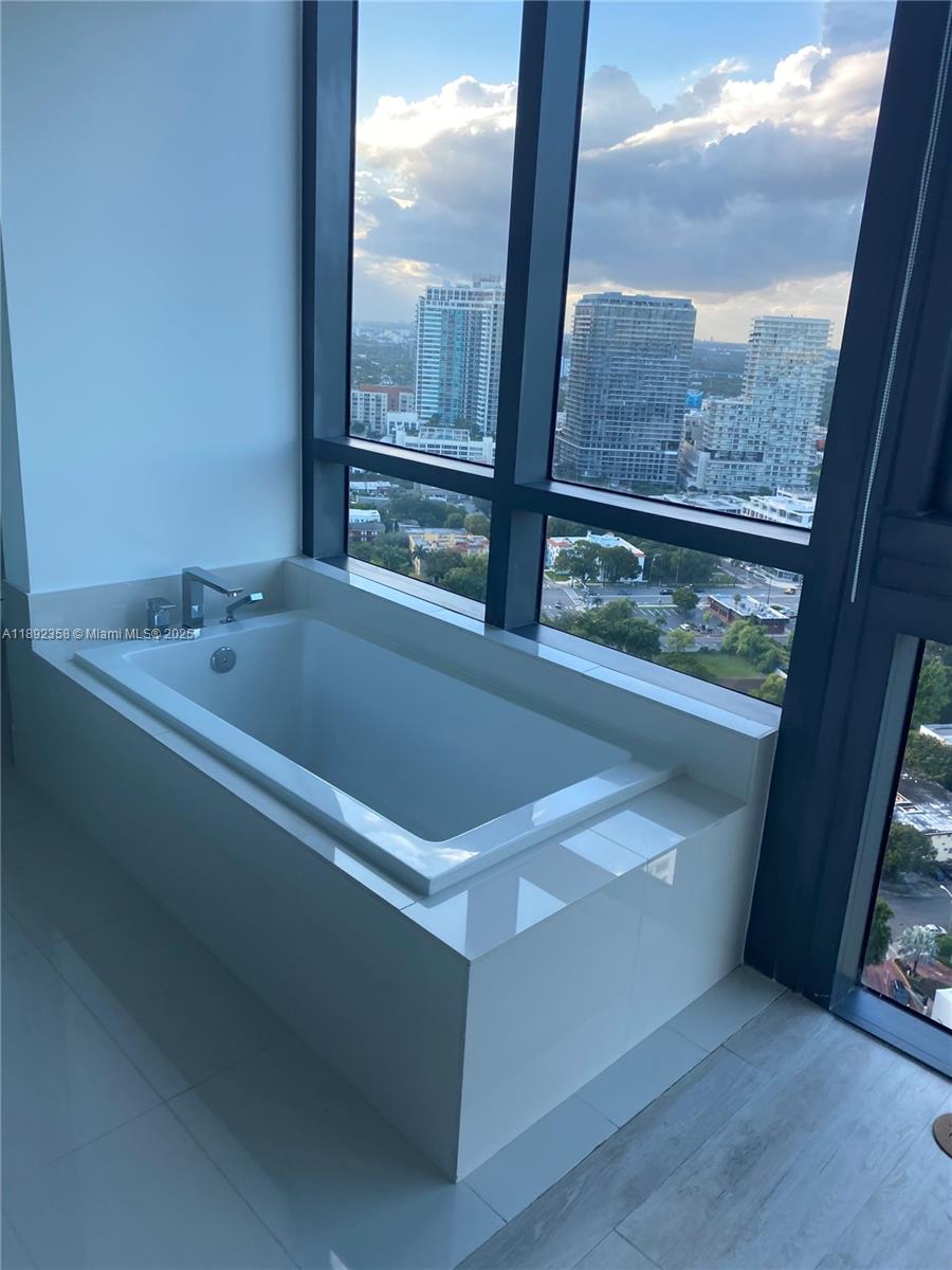 A white soaking tub sits next to floor-to-ceiling windows overlooking a city skyline — 650 NE 32nd St # 3108, Miami FL 33137, MIAMI, FL