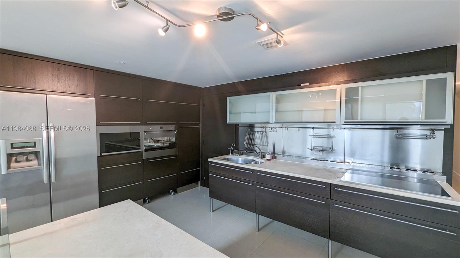 A modern kitchen features dark wood cabinetry, stainless steel appliances, and a white countertop — 6000 Collins Ave # 111, Miami Beach FL 33140, MIAMI BEACH, FL
