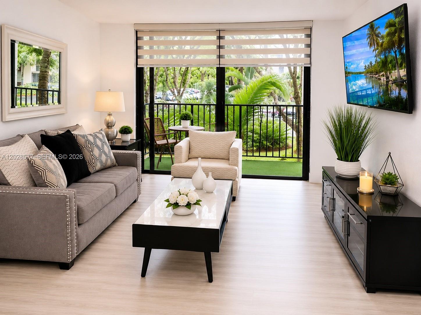 A living room features a gray sofa, a coffee table, and a balcony with greenery — 14311 N Kendall Dr # 206A, Miami FL 33186, MIAMI, FL