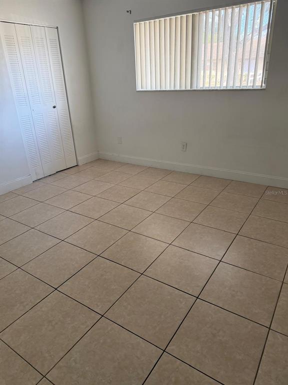 An empty room features light-colored floor tiles, white walls, a closet, and vertical window blinds — 500 E ROSEWOOD LANE UNIT 154, TAVARES, FL