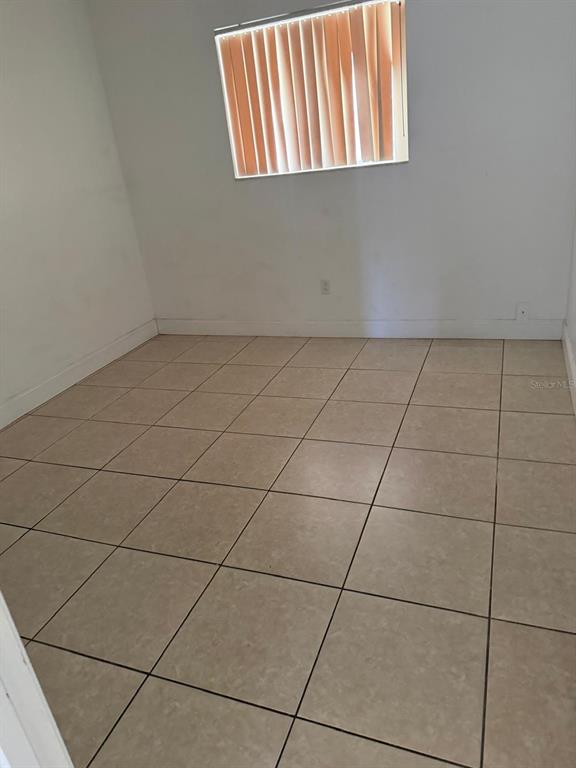 An empty room features light-colored tile flooring, white walls, and a window with vertical blinds — 500 E ROSEWOOD LANE UNIT 154, TAVARES, FL