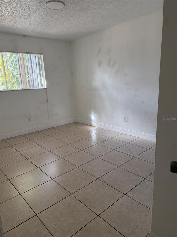 An empty room features light-colored floor tiles, white walls with visible patches, and a window — 500 E ROSEWOOD LANE UNIT 154, TAVARES, FL
