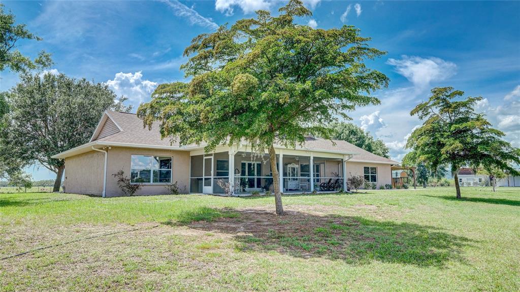 A tan house with a screened-in porch stands in a large, grassy yard with trees — 560 OAKFORD ROAD, SARASOTA, FL