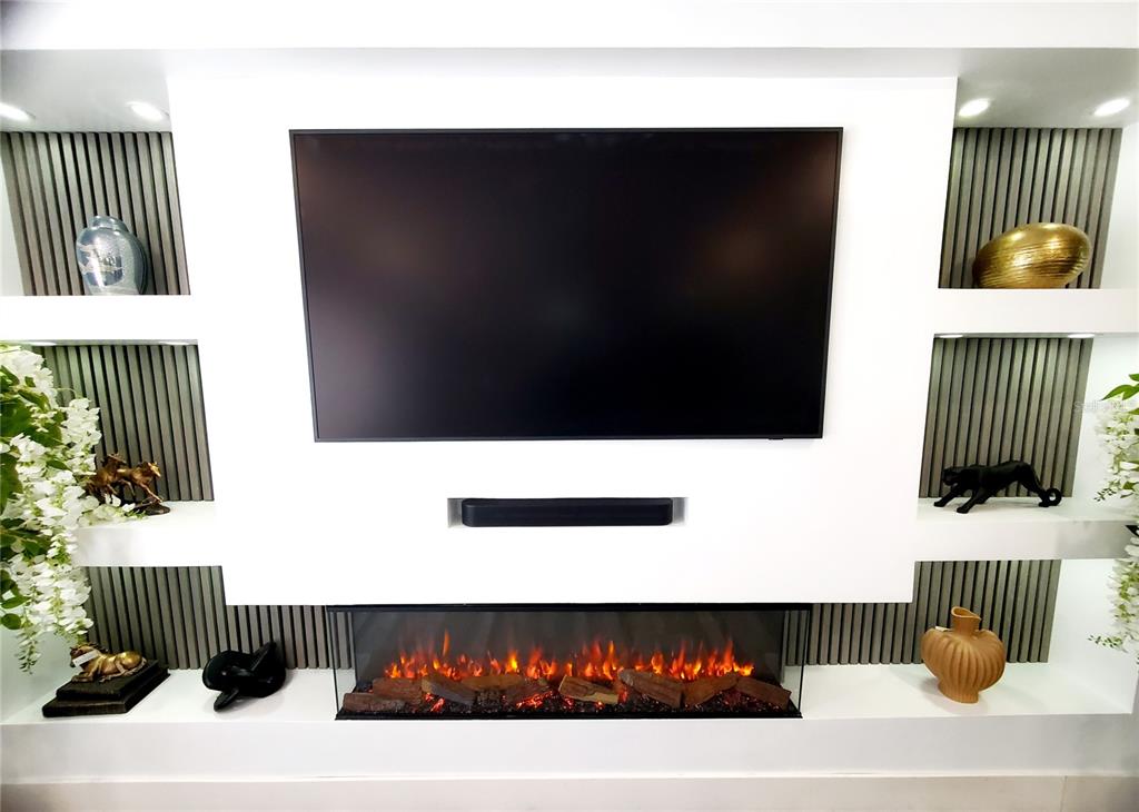A wall-mounted television sits above a linear electric fireplace in a modern living room — 2837 LONGLEAF LANE, PALM HARBOR, FL