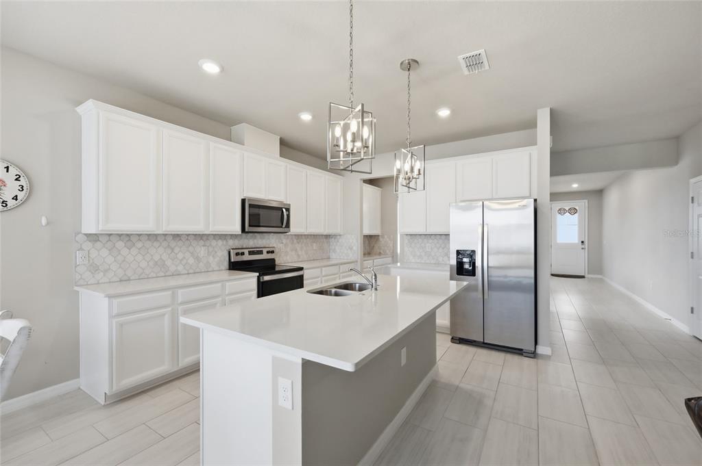A modern kitchen features white cabinetry, stainless steel appliances, a quartz island, and tile flooring — 2252 CROSSBOW STREET, CLERMONT, FL