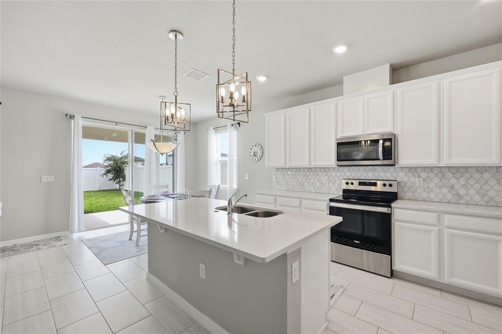 A modern kitchen features white cabinets, a central island, stainless steel appliances, and tile flooring — 2252 CROSSBOW STREET, CLERMONT, FL