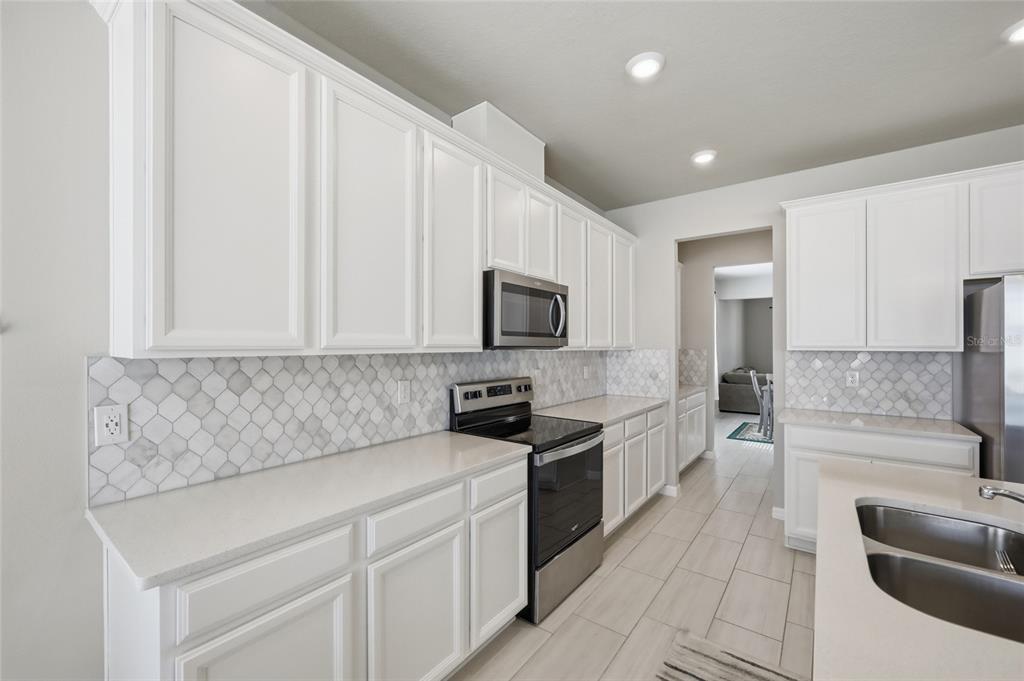 A kitchen features white cabinets, stainless steel appliances, a marble tile backsplash, and quartz countertops — 2252 CROSSBOW STREET, CLERMONT, FL