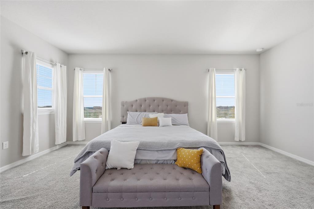 A bedroom features a tufted headboard, a matching bench, and three windows with white curtains — 2252 CROSSBOW STREET, CLERMONT, FL