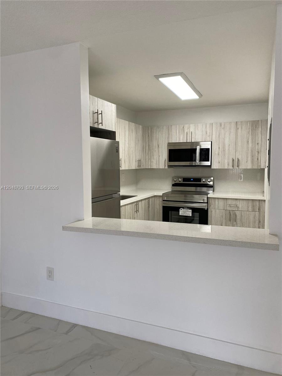 A kitchen features light wood-grain cabinets, stainless steel appliances, and a white quartz breakfast bar — 6190 W 19th Ave # 206, Hialeah FL 33012, HIALEAH, FL