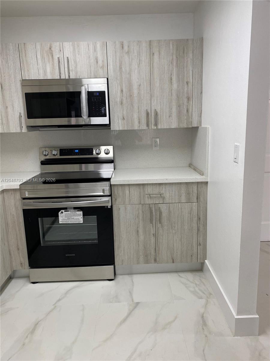 A kitchen features light wood-grain cabinets, stainless steel appliances, and white quartz countertops — 6190 W 19th Ave # 206, Hialeah FL 33012, HIALEAH, FL