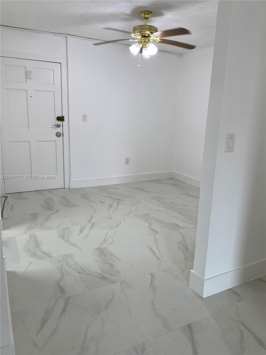 An empty room features white marble-look tile flooring, a ceiling fan, and a white door — 6190 W 19th Ave # 206, Hialeah FL 33012, HIALEAH, FL