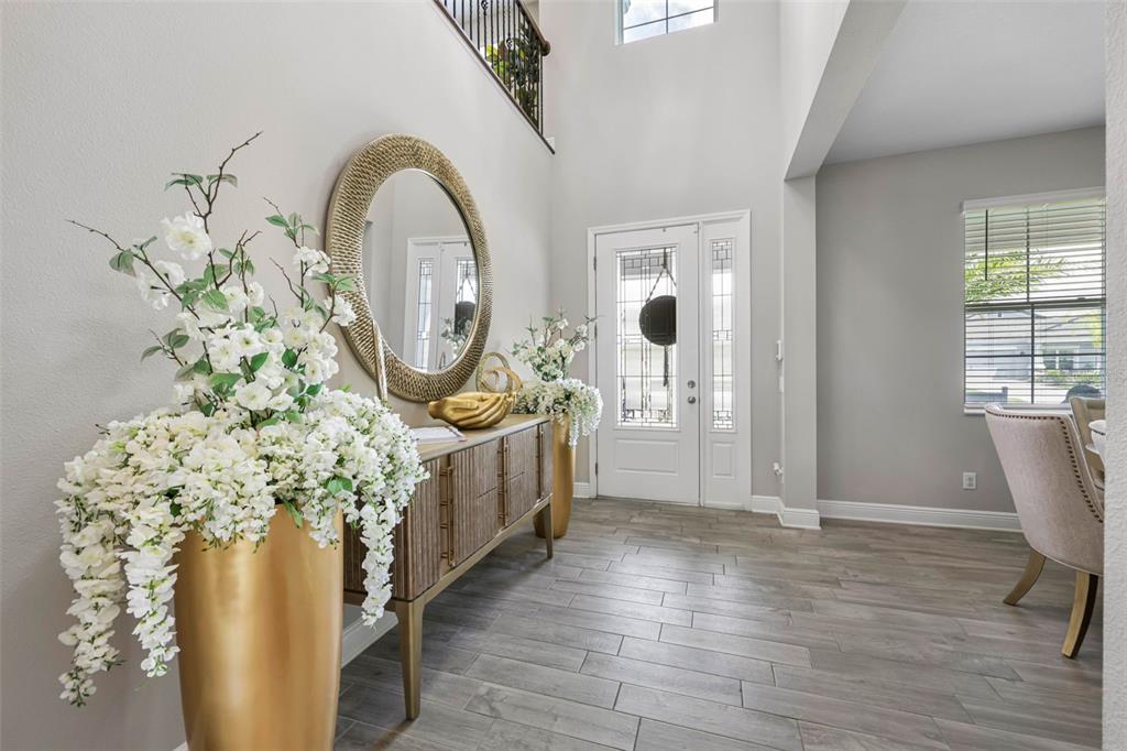 A bright entryway features a gold-toned console table, a large round mirror, and wood-look flooring — 38144 COBBLE CREEK BOULEVARD, ZEPHYRHILLS, FL