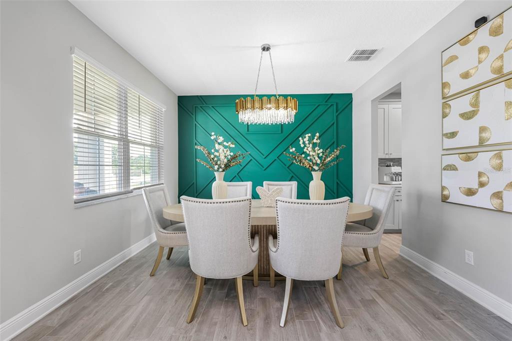 A dining room features a teal accent wall with geometric molding, a chandelier, and chairs — 38144 COBBLE CREEK BOULEVARD, ZEPHYRHILLS, FL