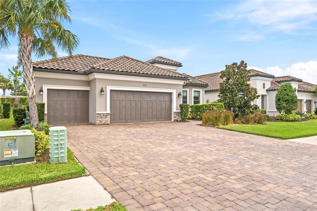A single-story house with a three-car garage and a paved driveway under a blue sky — 3118 FORSYTHIA DRIVE, ODESSA, FL
