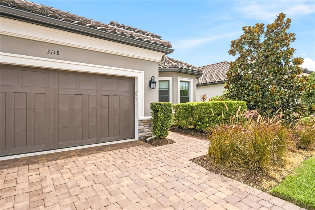 A paved driveway leads to a garage with a brown door and stone accents — 3118 FORSYTHIA DRIVE, ODESSA, FL