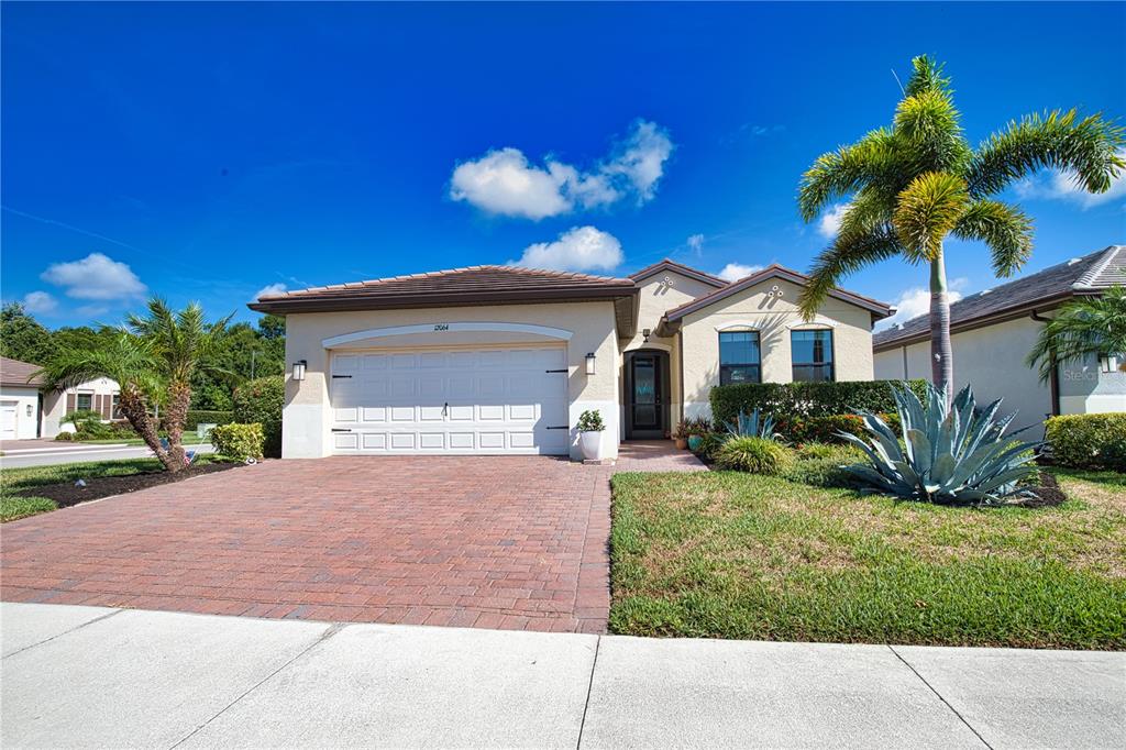 A single-story house with a brick paver driveway, a two-car garage, and a palm tree — 12064 BLAZING STAR DRIVE, VENICE, FL