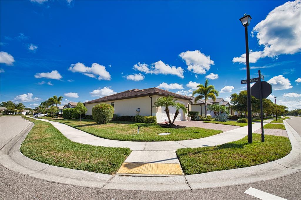 A corner lot features a single-story house with a tan exterior and a paved driveway — 12064 BLAZING STAR DRIVE, VENICE, FL