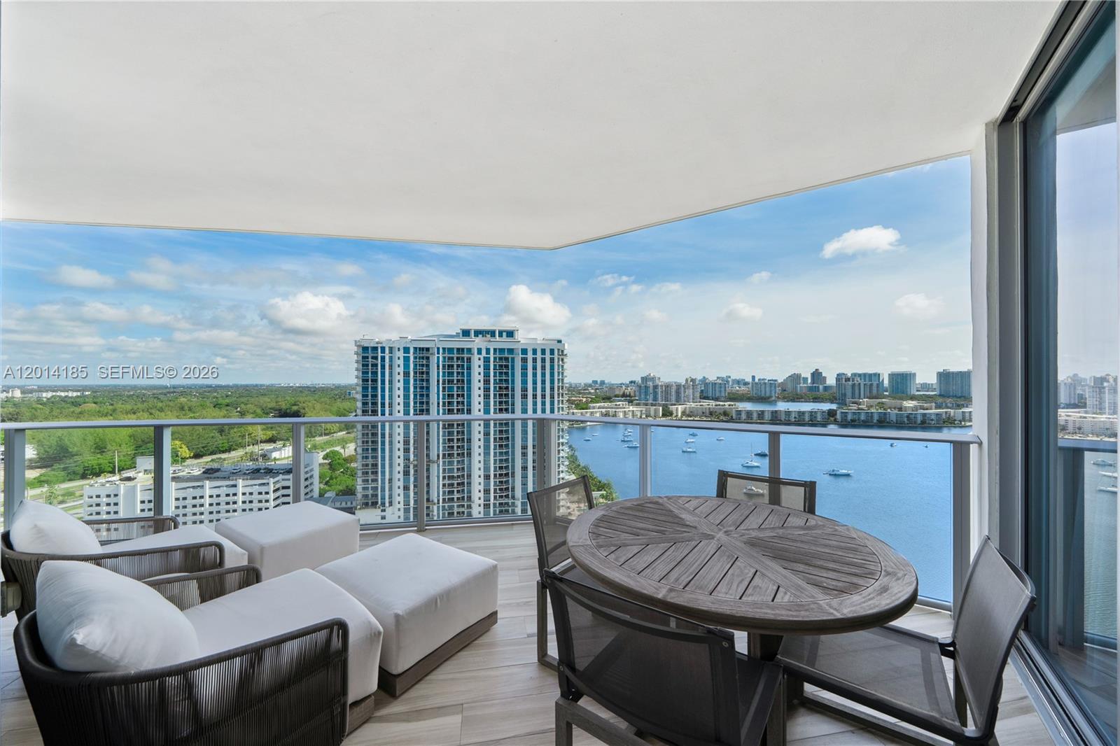 A balcony features outdoor furniture overlooking a bay, a high-rise building, and a green landscape — 17111 Biscayne Blvd # 2107, North Miami Beach FL 33160, NORTH MIAMI BEACH, FL