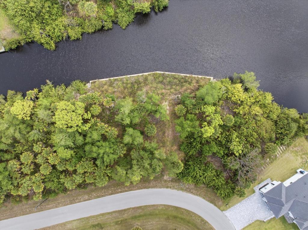 An aerial view shows a wooded waterfront lot with a concrete seawall along the canal — 554 MCDILL DRIVE, PORT CHARLOTTE, FL