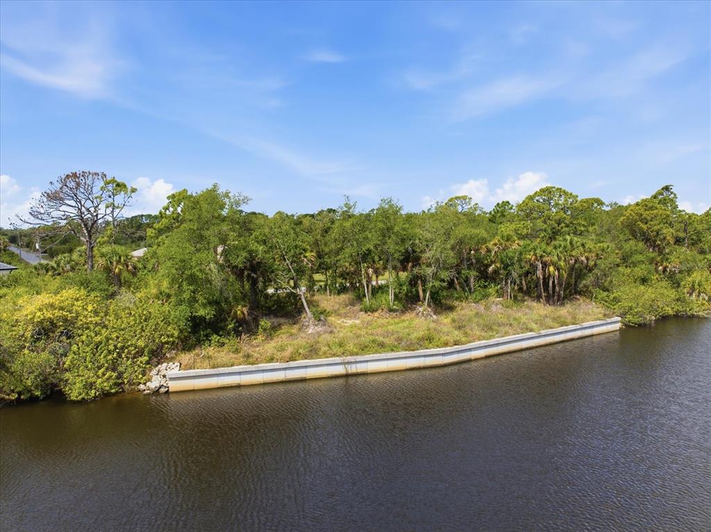 An aerial view shows a wooded waterfront lot with a concrete seawall along the canal — 554 MCDILL DRIVE, PORT CHARLOTTE, FL