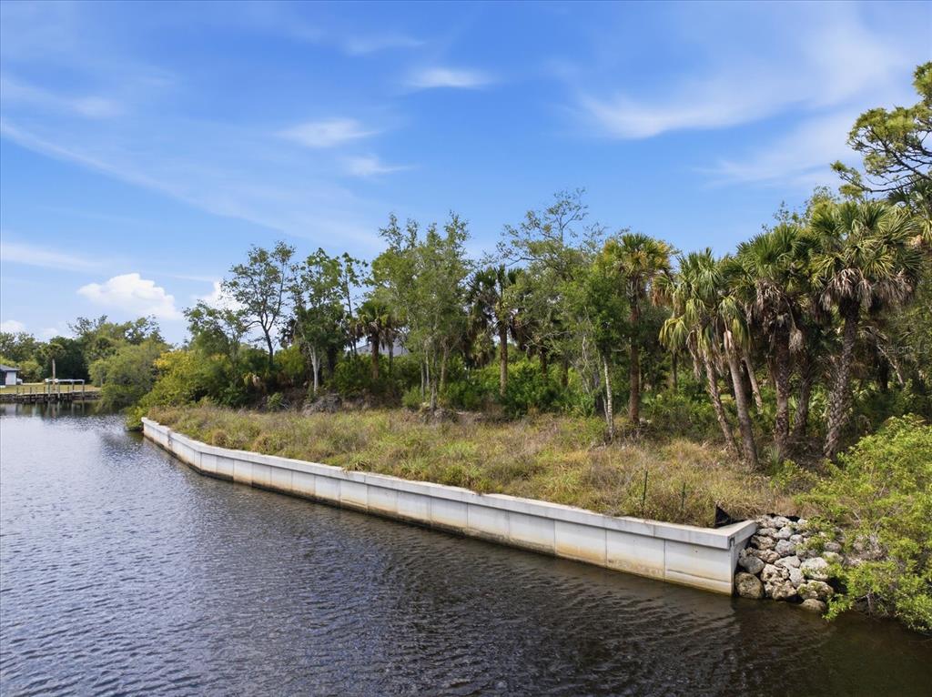 A concrete seawall borders a grassy, tree-filled waterfront lot along a canal — 554 MCDILL DRIVE, PORT CHARLOTTE, FL