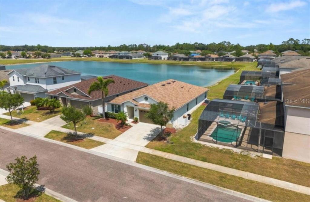 An aerial view shows a suburban house with a screened-in pool overlooking a lake — 4717 BLUE DIAMOND STREET, KISSIMMEE, FL