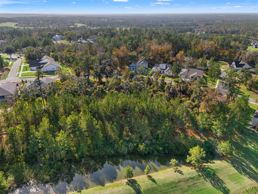 An aerial view shows a wooded lot situated next to a pond and residential neighborhood — 6633 SUMMIT VIEW DRIVE, BROOKSVILLE, FL