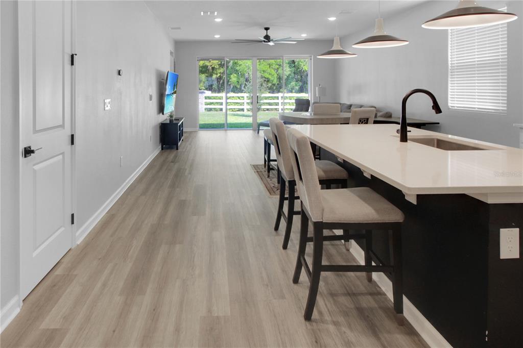 A kitchen island with bar stools overlooks an open-concept living area with sliding glass doors — 5208 MEADOW SONG DRIVE, OKAHUMPKA, FL