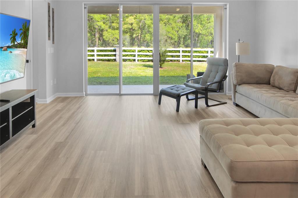 A living room with light wood flooring, a sofa, an armchair, and sliding glass doors — 5208 MEADOW SONG DRIVE, OKAHUMPKA, FL
