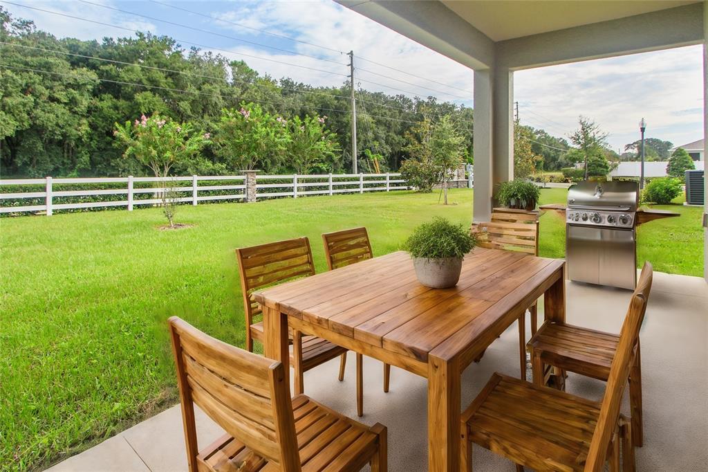 A covered patio features a wooden dining set, a grill, and a view of the yard — 5208 MEADOW SONG DRIVE, OKAHUMPKA, FL