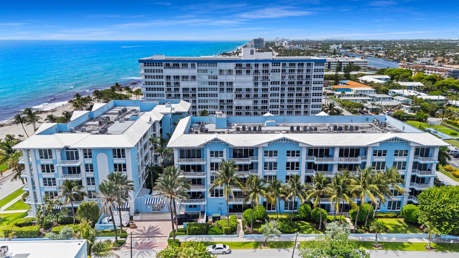 An aerial view shows a light blue multi-story apartment building located beside a sandy beach — 701 SE 21st Avenue # 501, Deerfield Beach FL 33441, DEERFIELD BEACH, FL