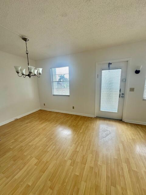 An empty room features light wood-look flooring, a chandelier, a window, and a glass-paneled door — 3063 Ainslie D, Boca Raton FL 33434, BOCA RATON, FL
