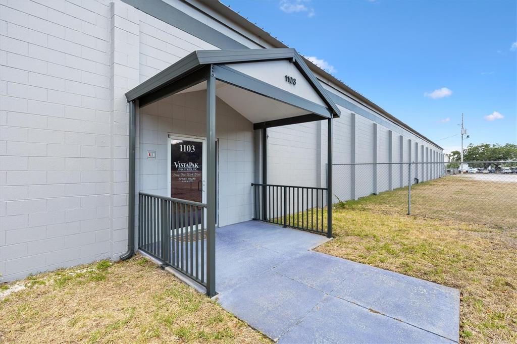 A gray concrete building entrance features a covered porch with a black metal railing — 1103 THOMAS AVENUE, LEESBURG, FL