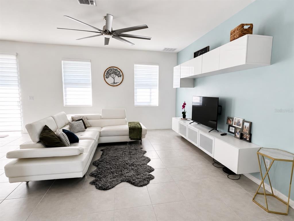 A modern living room features a white sectional sofa, a wall-mounted media console, and tile flooring — 3517 VEGA CREEK DRIVE, ST CLOUD, FL