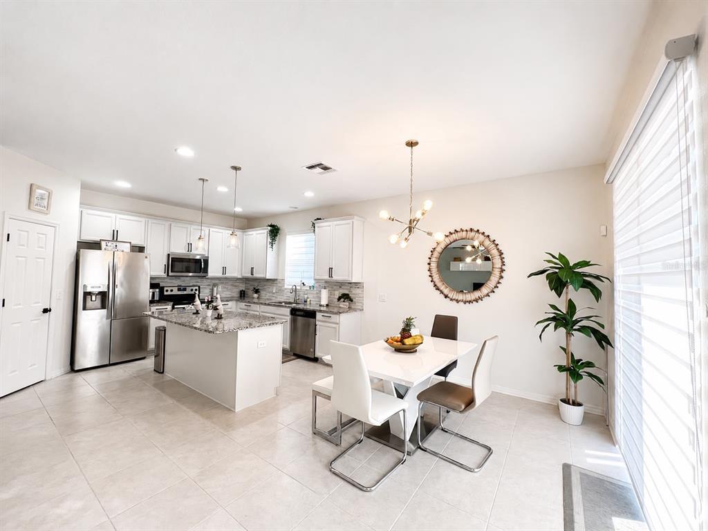 A bright kitchen and dining area features white cabinetry, granite countertops, and tile flooring — 3517 VEGA CREEK DRIVE, ST CLOUD, FL